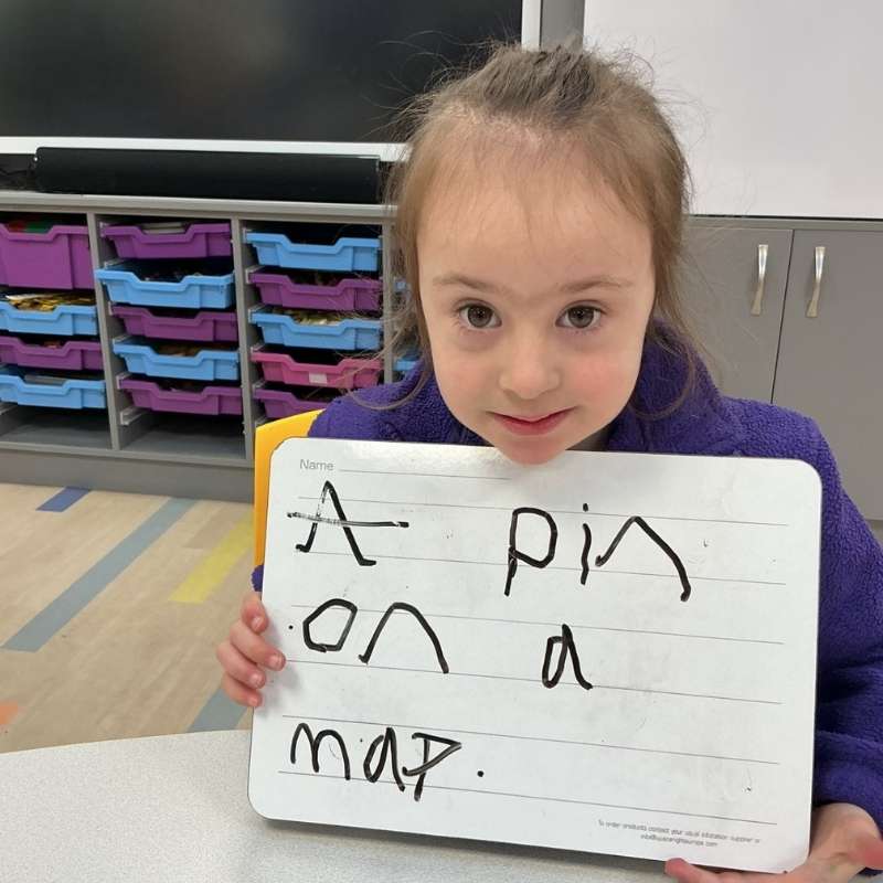 Child showing their writing on mini whiteboard 'A pin on a map'.