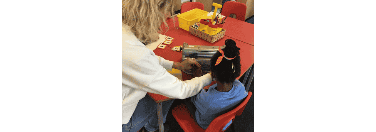 Adult helps child to place hands on brailler